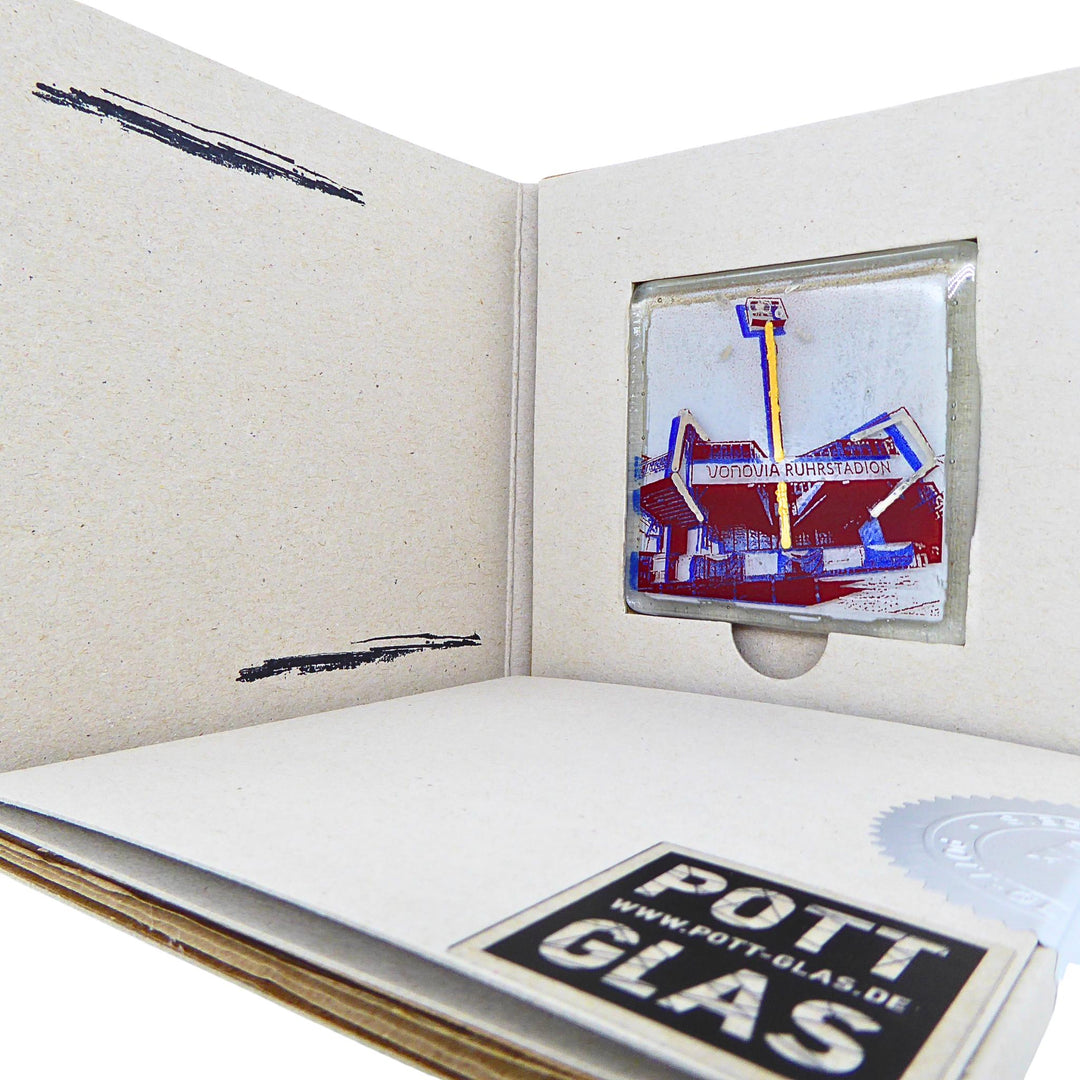 Bochum Edition 10/12. Geöffnete POTT GLAS Blanko-Inlay-Karte mit Beschriftungsfeld. Rechts ein Magnet-POTTRÄT aus Schmelzglas mit blauem Ruhrstadion-Motiv sowie Akzenten aus 24-Karat-Flüssiggold und Platin im Karten-Inlay mit Entnahmeaussparung. Darunter die versiegelte Karte mit Logo und geprägter Siegelplombe.