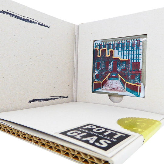 Bochum Edition 11/12. Geöffnete POTT GLAS Blanko-Inlay-Karte mit Beschriftungsfeld. Rechts ein Magnet-POTTRÄT aus Schmelzglas mit grünem Haus Weitmar-Motiv sowie Akzenten aus 24-Karat-Flüssiggold und Platin im Karten-Inlay mit Entnahmeaussparung. Darunter die versiegelte Karte mit Logo und geprägter Siegelplombe.
