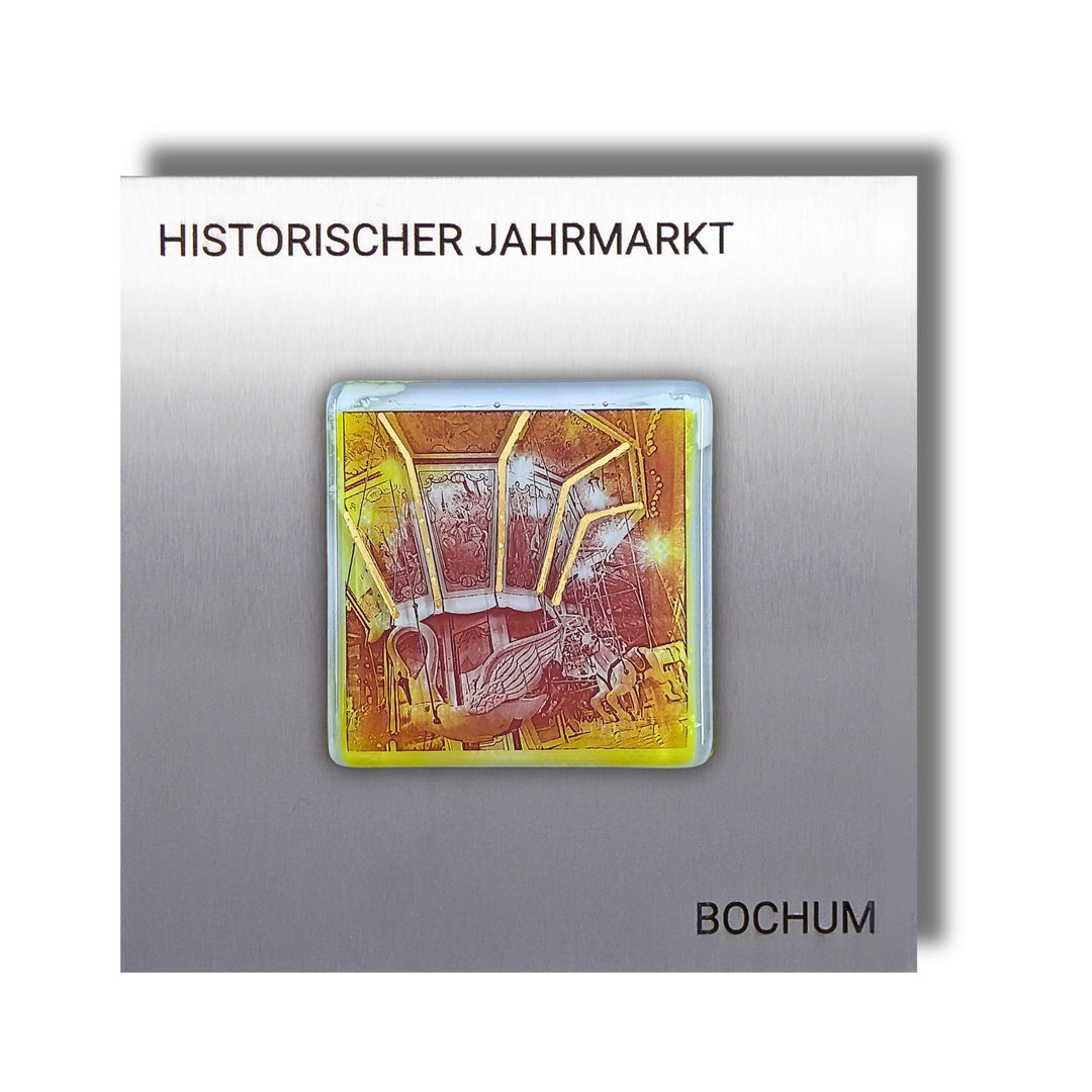 Edition 3/12. Pott Glas Wand-Potträt mit Karussellschwan-Motiv in Gelb mit Gold und Platin Akzenten. Foto in Schmelzglas auf Edelstahl. Quadratisches Format mit Gravur „Historischer Jahrmarkt Bochum“.