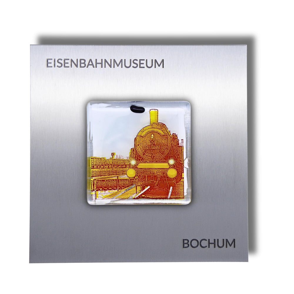 Edition 5/12. Pott Glas Wand-Potträt mit Dampflok-Motiv in Gelb. Foto in Schmelzglas auf Edelstahl. Quadratisches Format mit Gravur „Eisenbahnmuseum Bochum“.