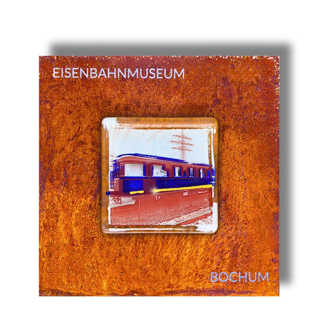 Edition 5/12. Pott Glas Wand-Potträt mit Railflex-Motiv in Blau. Foto in Schmelzglas auf Roststahl. Quadratisches Format mit Gravur „Eisenbahnmuseum Bochum“.
