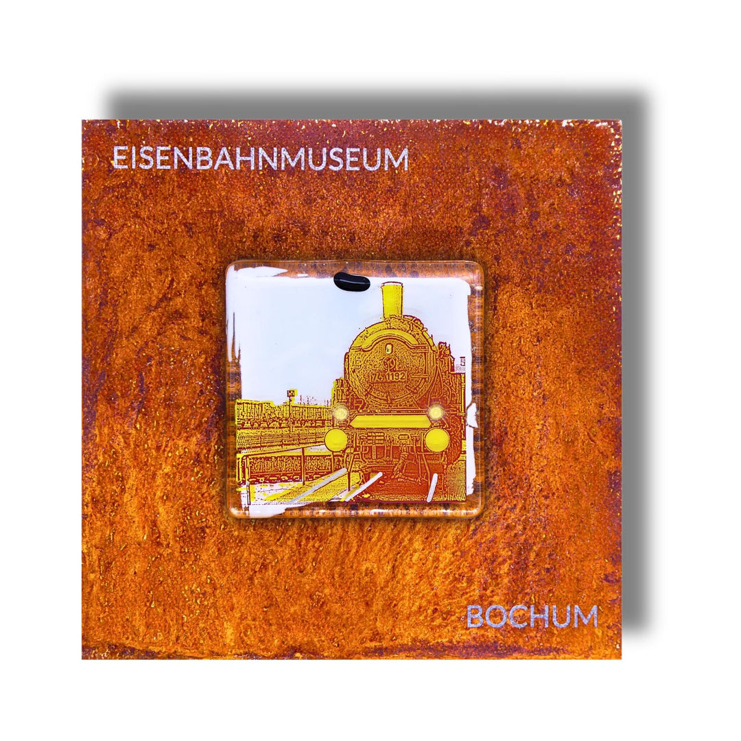 Edition 5/12. Pott Glas Wand-Potträt mit Dampflok-Motiv in Gelb. Foto in Schmelzglas auf Roststahl. Quadratisches Format mit Gravur „Eisenbahnmuseum Bochum“.