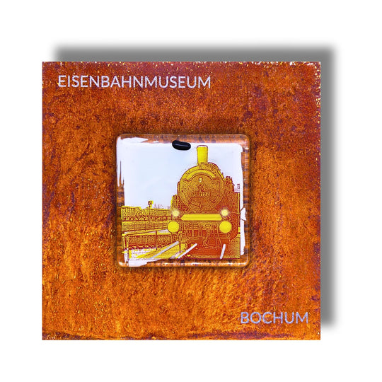 Edition 5/12. Pott Glas Wand-Potträt mit Dampflok-Motiv in Gelb. Foto in Schmelzglas auf Roststahl. Quadratisches Format mit Gravur „Eisenbahnmuseum Bochum“.