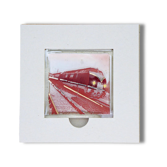 Bochum Edition 05/12. Offenes POTT GLAS Karten-Inlay mit quadratischer Aussparung und Entnahmeaussparung. Darin ein Magnet-POTTRÄT aus Schmelzglas mit V-Dieselzug-Motiv in Rot sowie Akzenten aus 24-Karat-Flüssiggold und Platin.