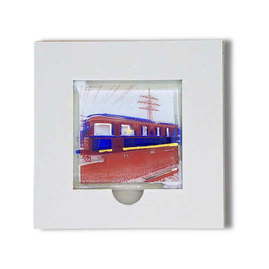 Bochum Edition 05/12. Offenes POTT GLAS Karten-Inlay mit quadratischer Aussparung und Entnahmeaussparung. Darin ein Magnet-POTTRÄT aus Schmelzglas mit Railflex-Partywagen-Motiv in Blau sowie Akzenten aus 24-Karat-Flüssiggold und Platin.