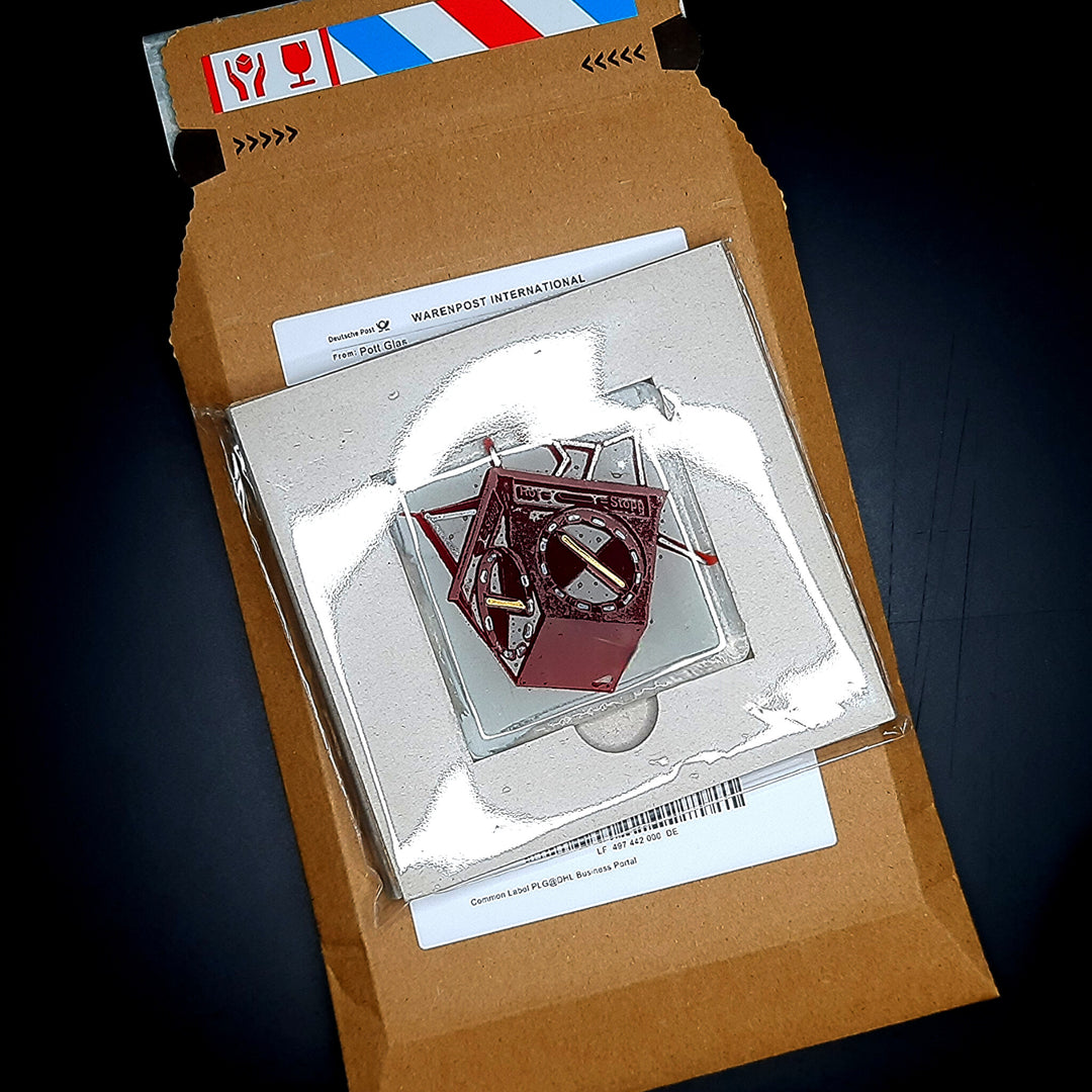 Bild 1 · offene Verpackung. 
POTT GLAS Magnet-Potträt Verpackungsansicht am Beispiel der roten Heuer-Ampel. Zeigt Inlay-Karte mit Schmelzglas-Magnet in Schutzhülle und bruchsicherer Karton-Umverpackung für den Briefkasten-Versand. 