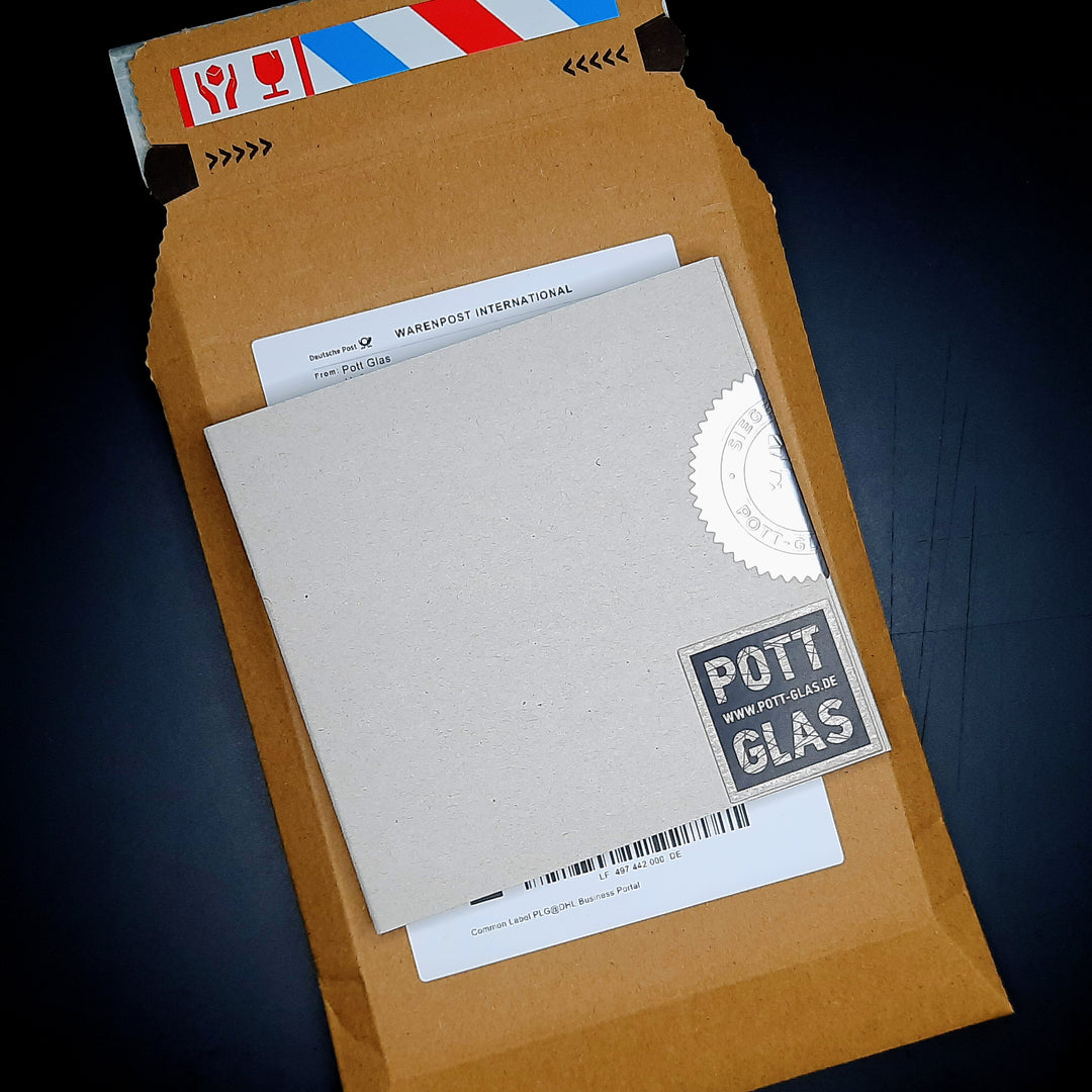 Bild 2 · versiegelte Verpackung. POTT GLAS Magnet-Potträt Verpackungsansicht. Zeigt die versiegelte Inlay-Karte mit POTT GLAS Logo und geprägter Siegelplombe in der bruchsicher geschützten Karton-Umverpackung für den Briefkasten-Direktversand.