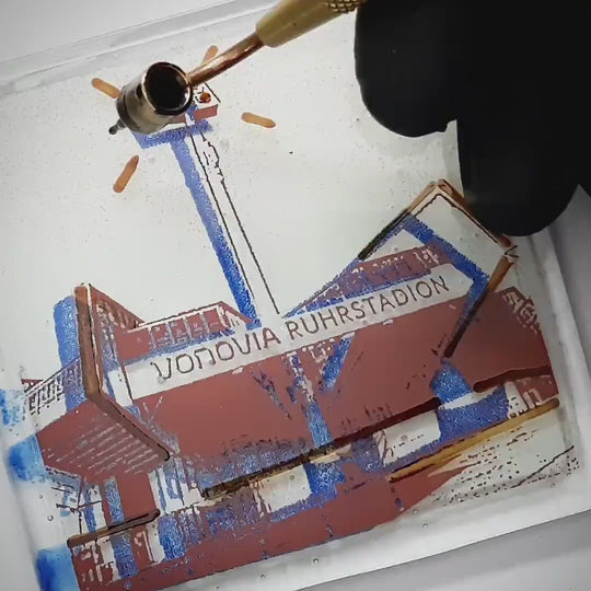 Pott Glas Produktvideo. Zeigt das manuelle Setzen von Akzenten am „Ruhrstadion“-Glasbild mit Flüssiggold und Platin.